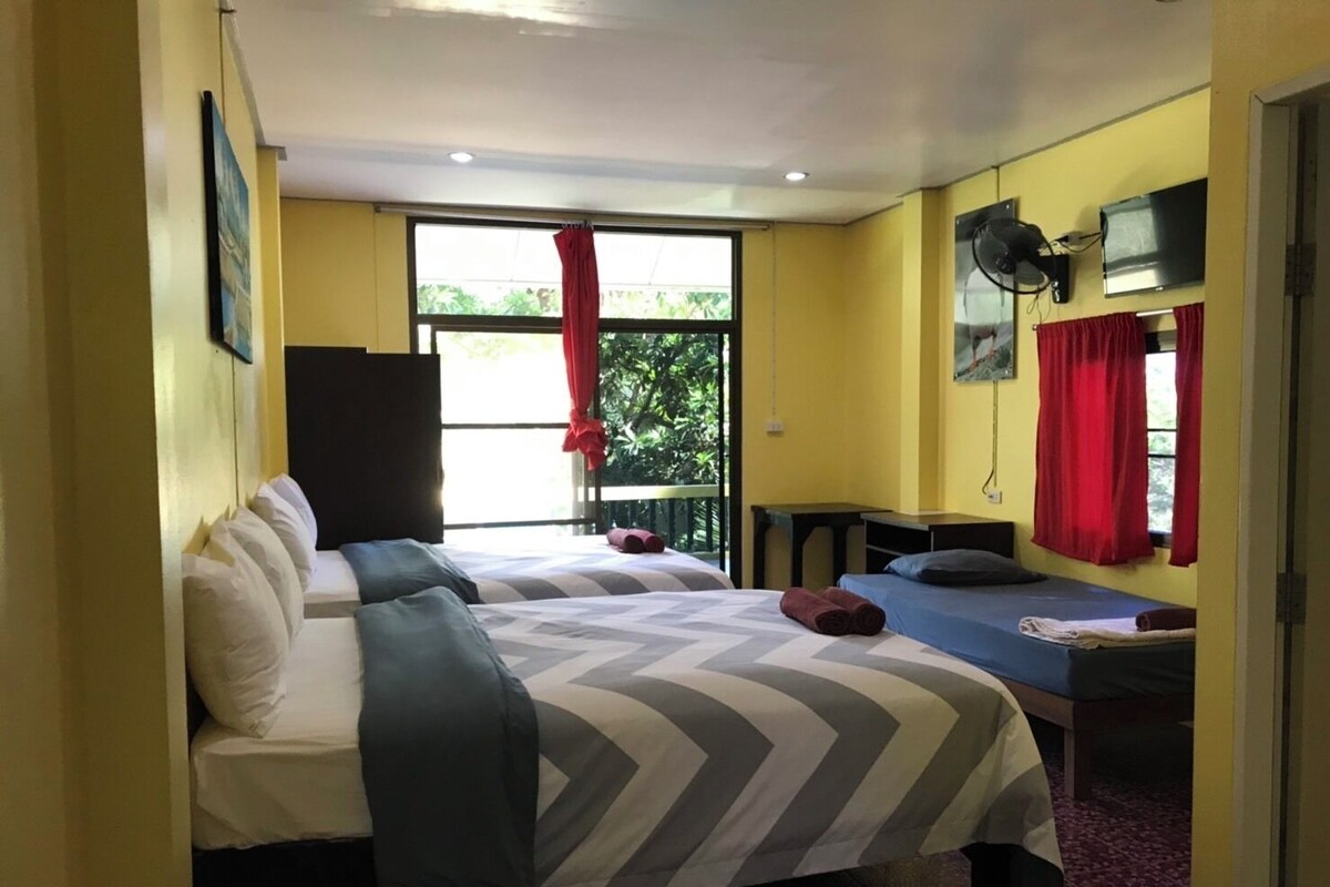 A room with two beds, a TV, and a window with red curtains.