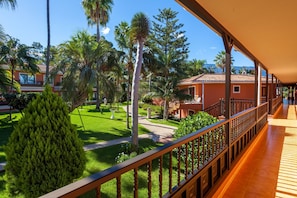 A balcony with a wooden railing overlooking a well-maintained garden with palm trees and a pathway.