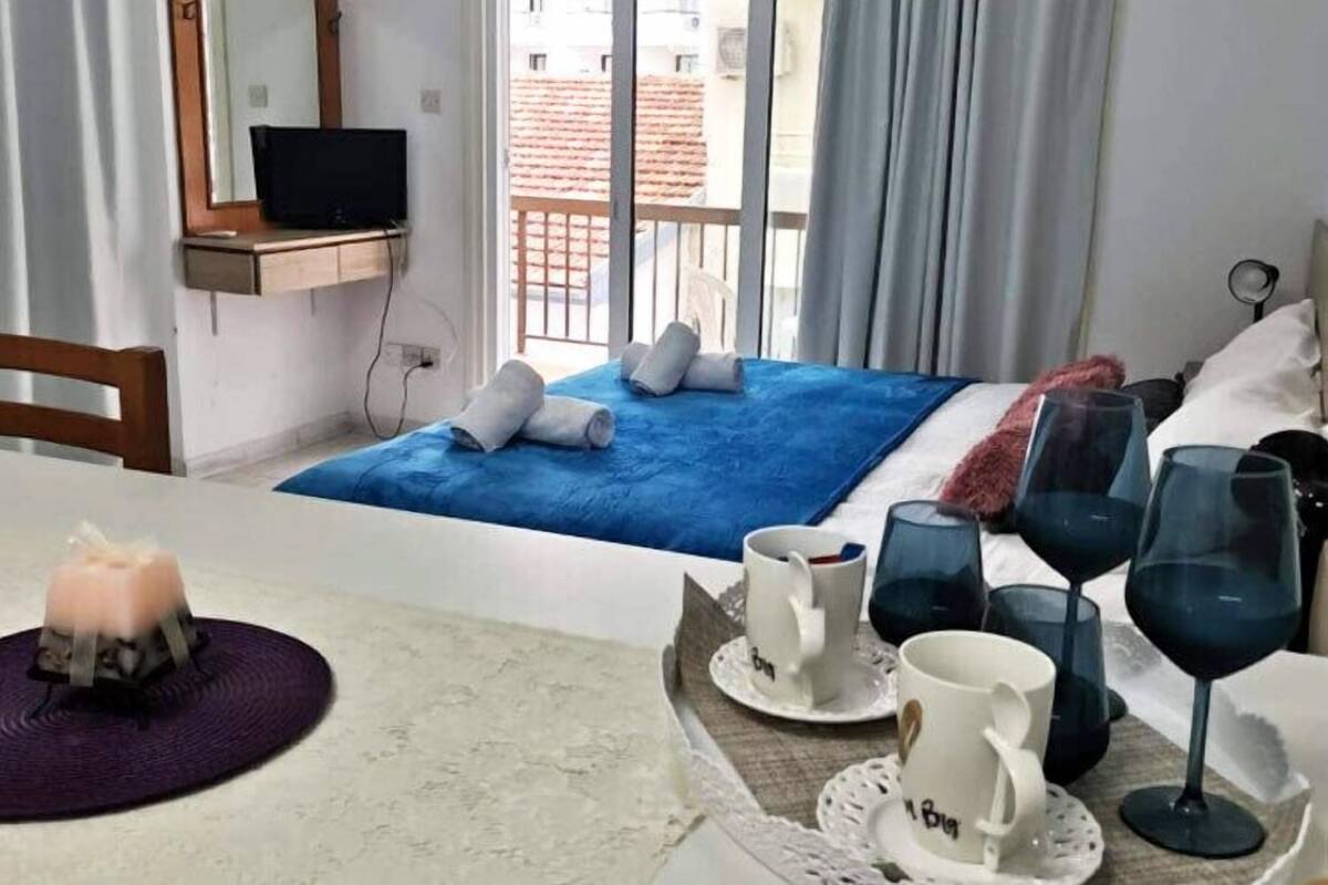 A hotel room with a bed, a TV, a balcony with towels, and a table with wine glasses and a candle.
