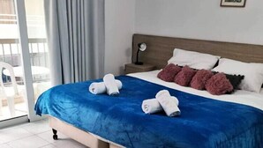 A hotel room with a large bed, a nightstand, a chair, and a view of the outside. - Palm Sea Hotel Apartments 2 (Larnaca)