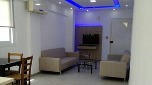 A modern living room with a sofa, a dining table with chairs, and a TV mounted on the wall. - Palm Sea Hotel Apartments 2 (Larnaca)