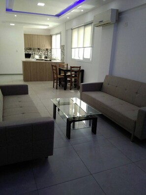 A modern living room with a glass coffee table, a sofa, and a dining area with chairs and a table.