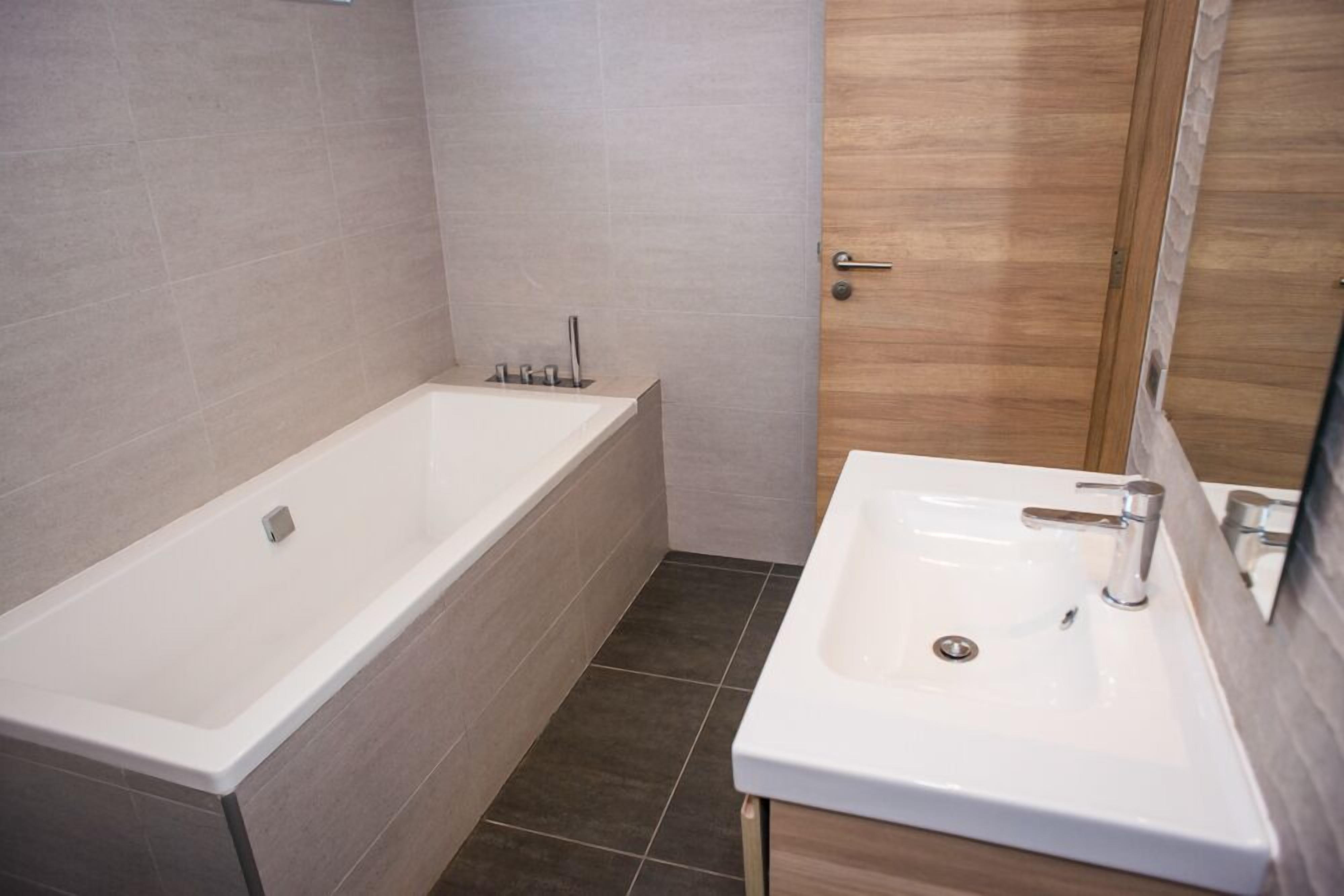 A modern bathroom with a bathtub, a sink, and a wooden door.