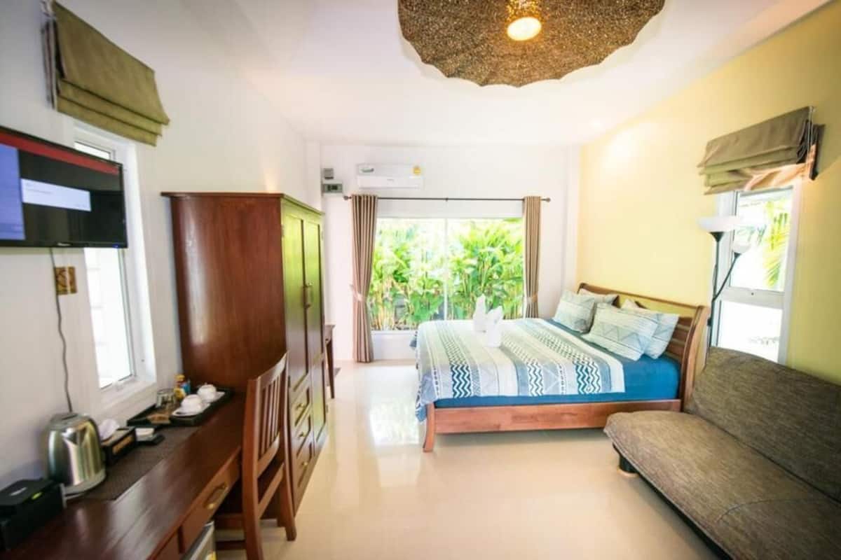 Un dormitorio con cama, cómoda de madera, sofá, televisor y ventana con cortinas.