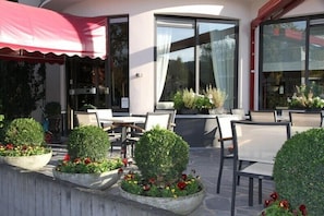 An outdoor seating area with tables and chairs, surrounded by neatly trimmed hedges and flower beds. - Hotel Limburgia (Riemst)