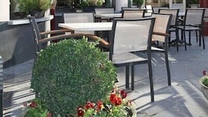 Een buitenzitgedeelte met tafels en stoelen, potplanten en een toegang tot een gebouw.