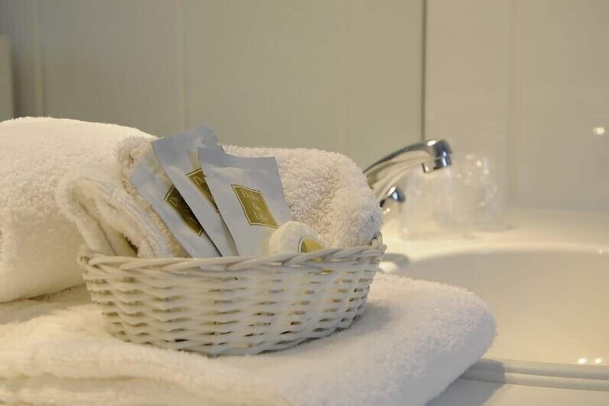 Une serviette blanche et un panier contenant des articles de toilette sont posés sur le lavabo de la salle de bain.