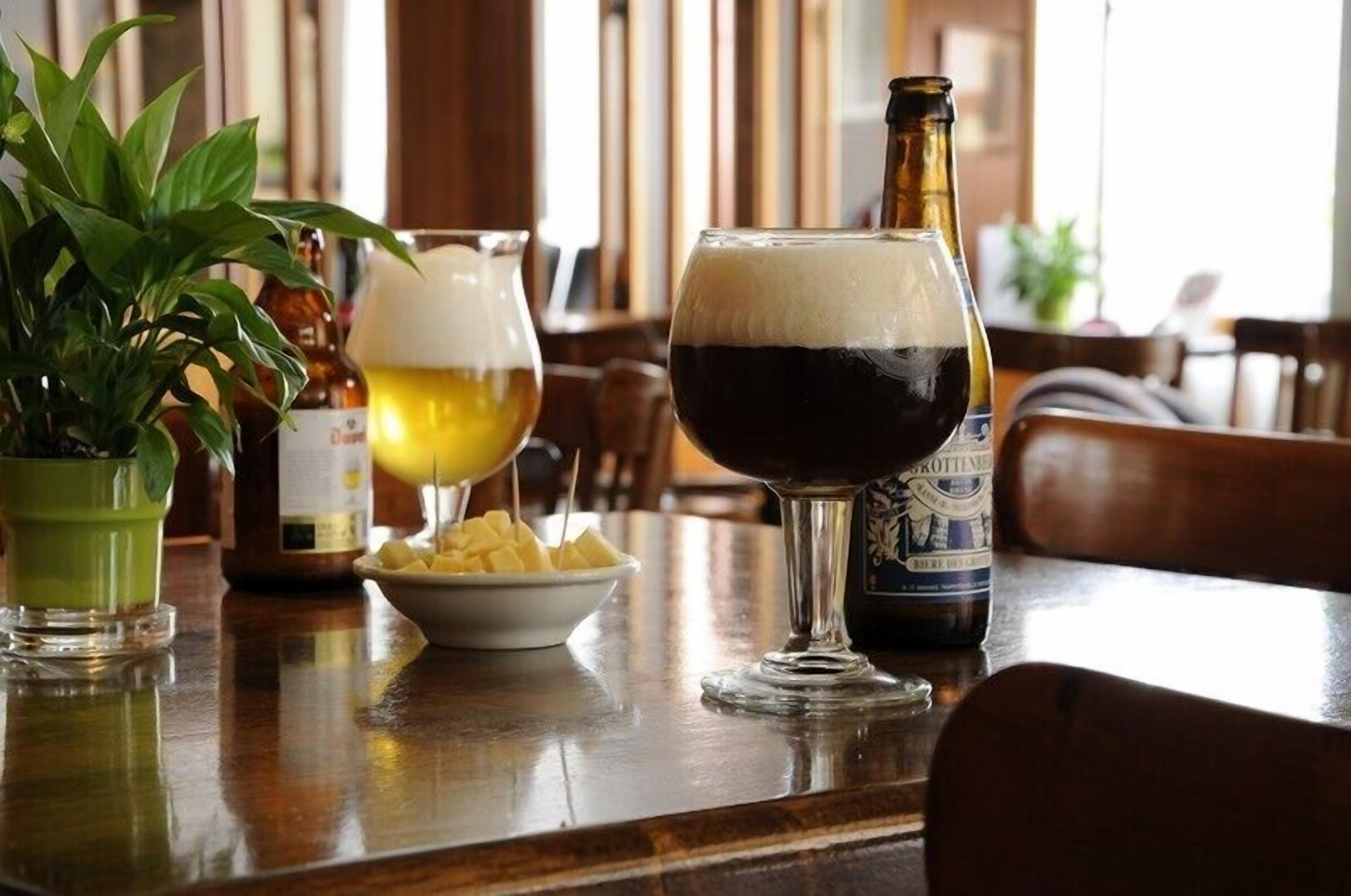 Um bar com uma garrafa de cerveja, um copo de cerveja e um copo de cerveja escura sobre uma mesa de madeira.
