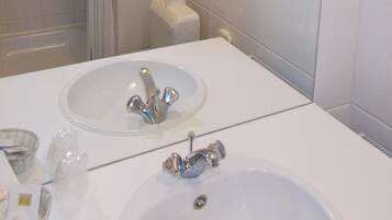 Une salle de bain moderne avec une douche à parois de verre, un lavabo blanc avec un miroir et des toilettes équipées d’un distributeur de serviettes en papier.