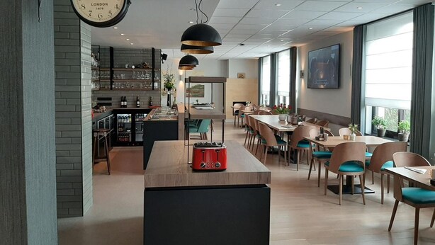 Een moderne eetruimte met een lange houten tafel, meerdere stoelen en een keuken met een bakstenen muur en planken.