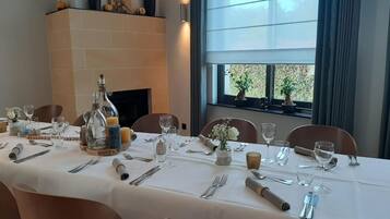 A dining table set for a meal with a fireplace in the background and a window with plants.