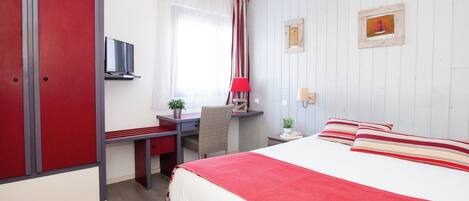 Ett hotellrum med en säng, ett skrivbord, en stol, en tv och ett fönster med gardiner.