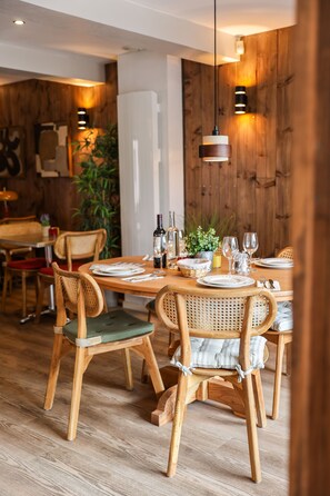 A dining area with wooden tables and chairs, a potted plant, and a white refrigerator. - Hotel Restaurant Atlantide (Biscarrosse)