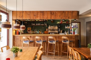 A bar area with wooden furniture, bar stools, shelves with bottles, and a counter. - Hotel Atlantide (Biscarrosse)