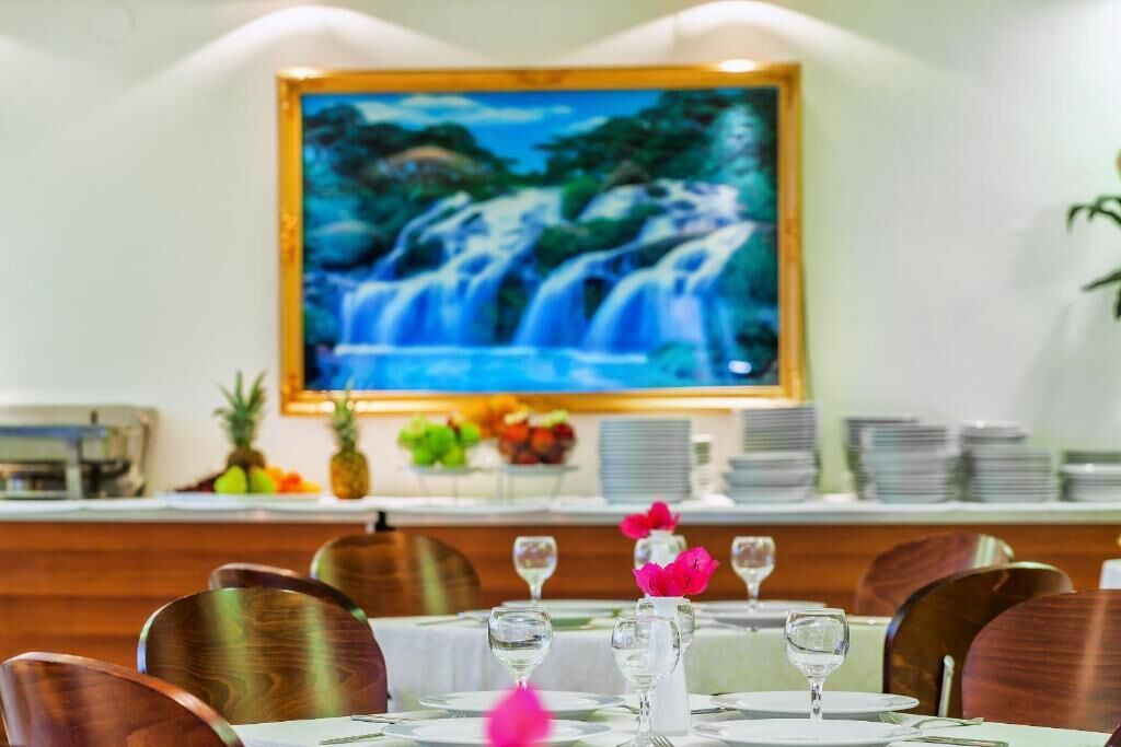 A restaurant with a waterfall painting on the wall, wooden chairs, and a table set with wine glasses and plates.