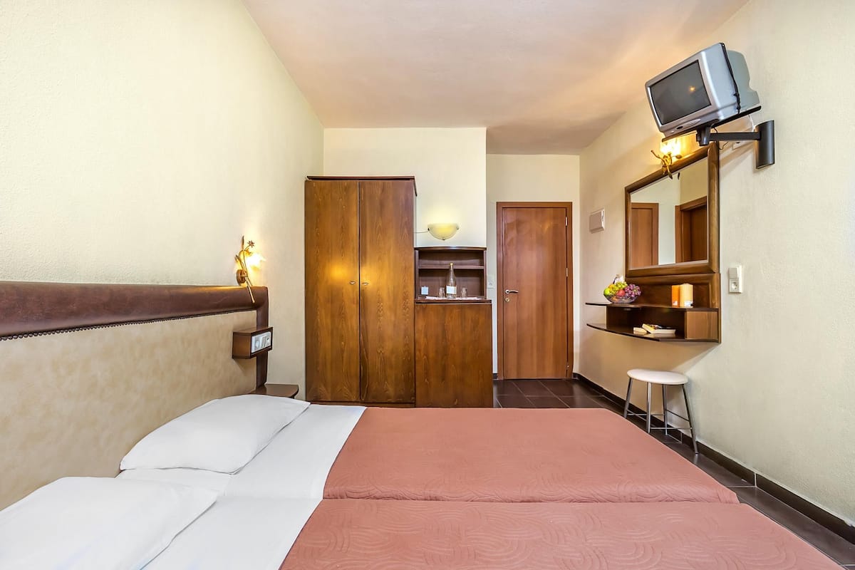 Una habitación de hotel con una cama, un armario de madera, un escritorio pequeño con un espejo y un televisor montado en la pared.