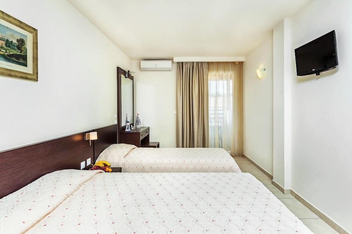 Una habitación de hotel con dos camas, televisión, escritorio con lámpara y ventana con cortinas.