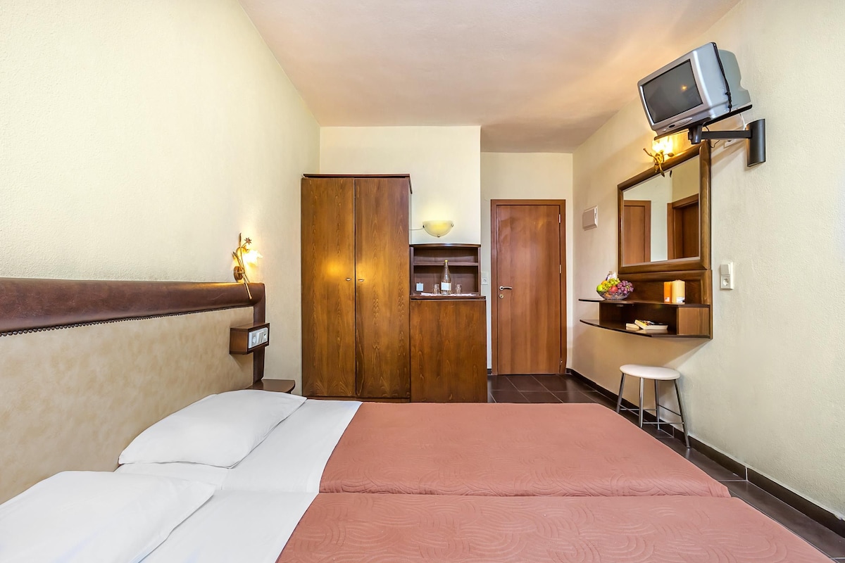 Una habitación de hotel con una cama, un armario de madera, un escritorio pequeño con un espejo y un televisor montado en la pared.
