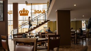 A restaurant interior with wooden tables and chairs, a staircase, and large windows. - Hotel Cisar (Lviv)
