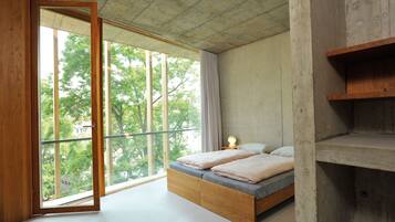 A bedroom with a large window, a bed, and a wooden shelf.