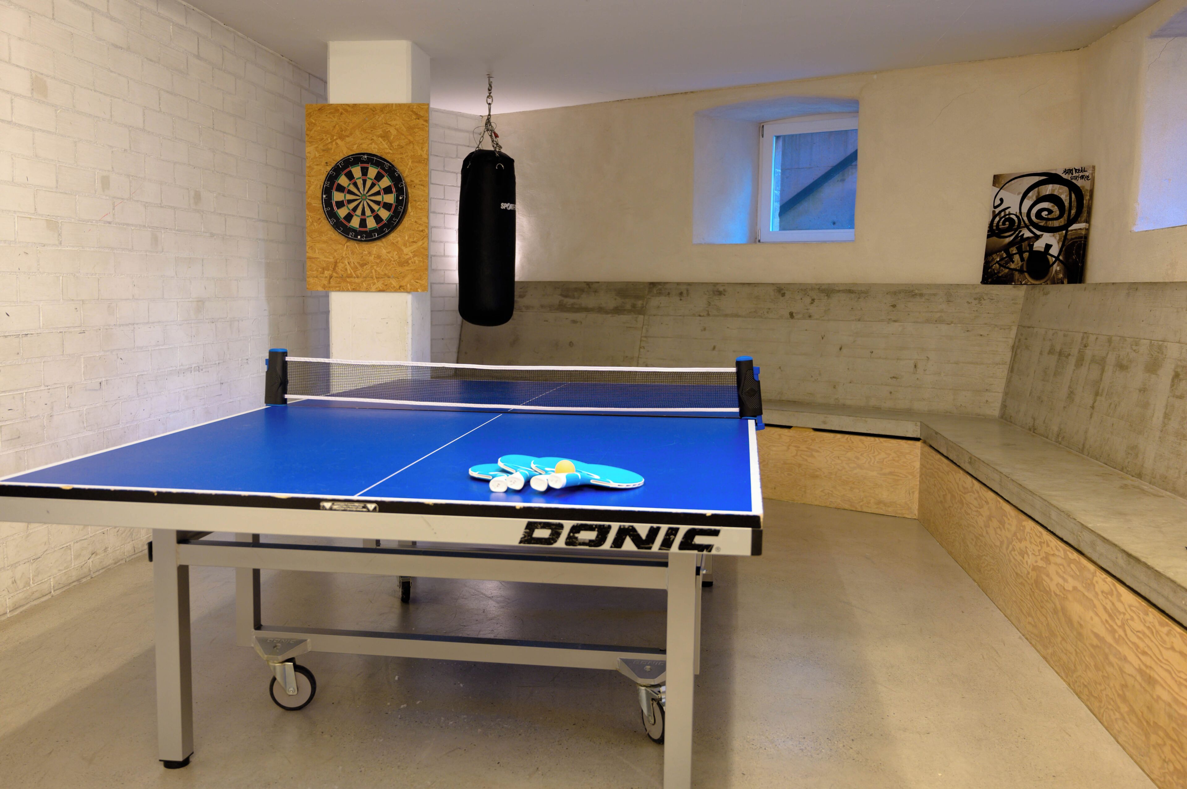 A ping pong table with a net, a punching bag, and a dartboard on the wall.