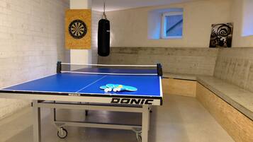 A ping pong table with a net, a punching bag, and a dartboard on the wall.