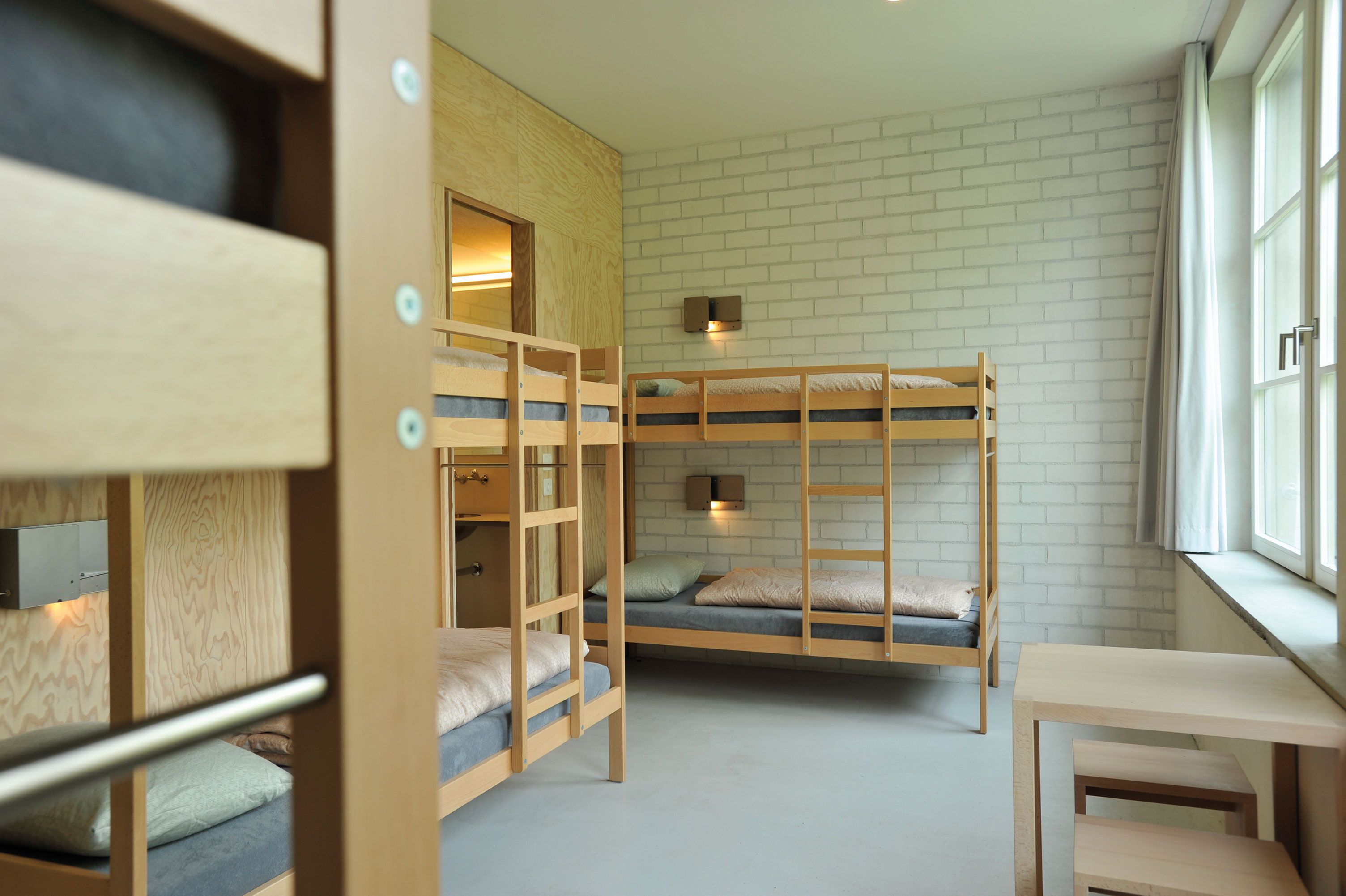 A room with bunk beds, a small table, and a window with curtains.