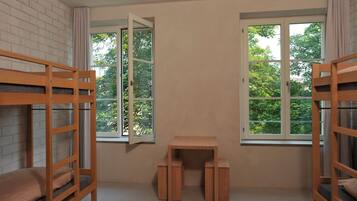 A room with bunk beds, a small wooden table, and two windows with curtains.