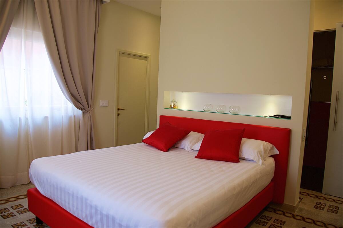 A neatly made bed with red and white bedding, a glass shelf above it, and a patterned floor.