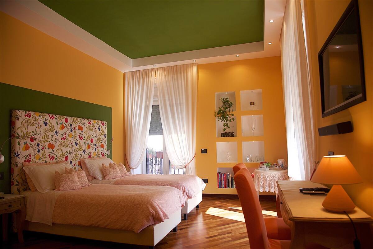 A bedroom with two beds, a desk with a lamp, a chair, and a bookshelf with books and decorative items.