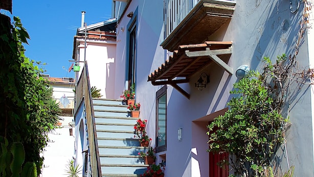 Eine schmale Gasse mit einer Treppe, die zu einem Gebäude mit Balkonen und Kübelpflanzen führt.