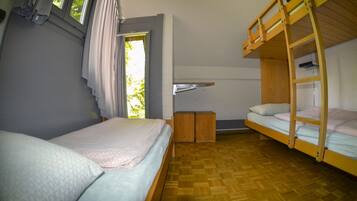 Een kamer met twee stapelbedden, een klein houten kastje en een raam met gordijnen.