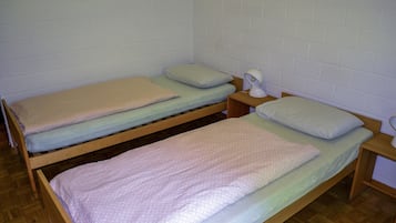 Ein kleines, sauberes Zimmer mit zwei Holzbettgestellen übereinander, jeweils mit Kissen und einer Nachttischlampe.