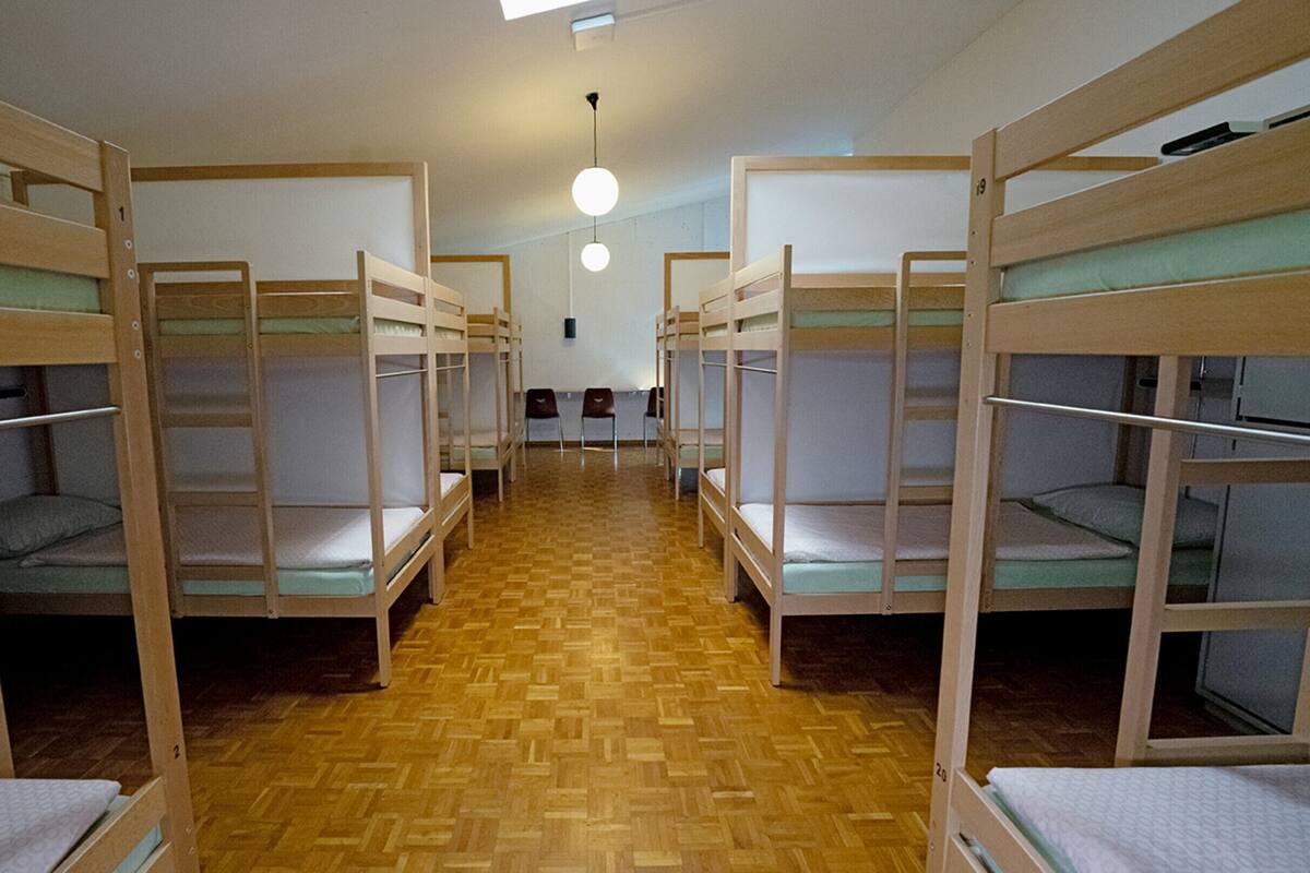 Un dormitorio con literas dispuestas en filas, suelo de madera y una lámpara central.