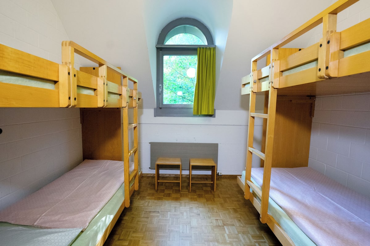 Un dormitorio con literas, una ventana con cortinas y una mesita pequeña.