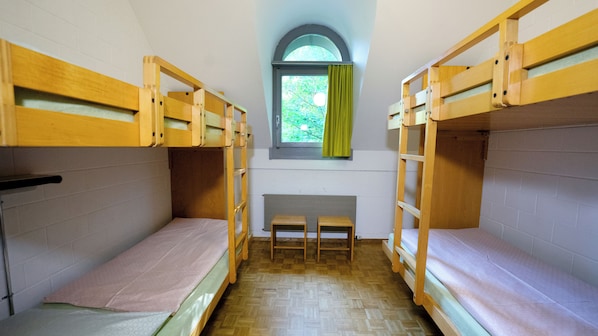A dormitory room with bunk beds, a window with curtains, and a small table. - Youth Hostel Luzern (Lucerne)