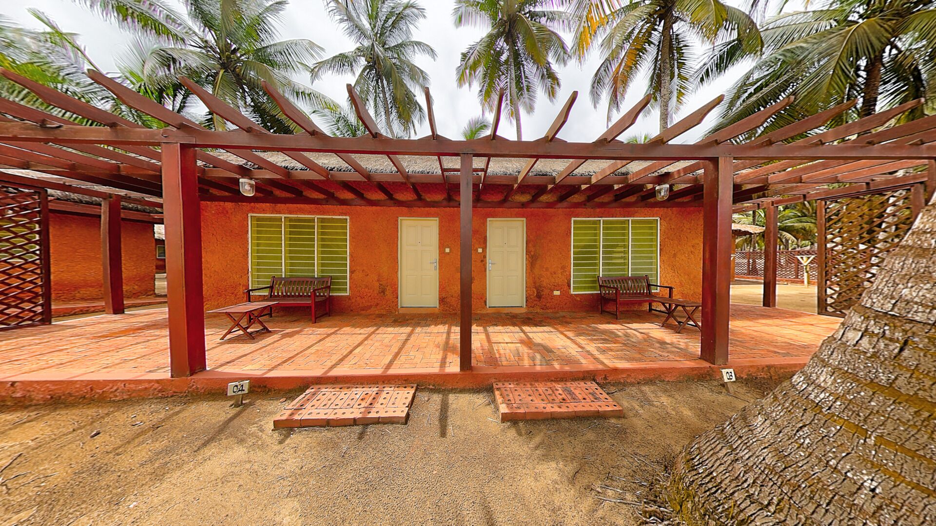 A covered outdoor area with benches and doors, surrounded by palm trees.