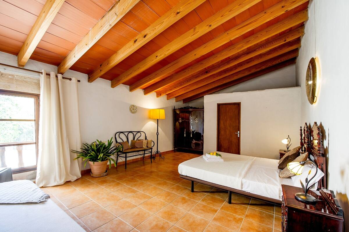 Une chambre avec un plafond en bois, un lit, une table de chevet avec une lampe, une chaise et une plante en pot.