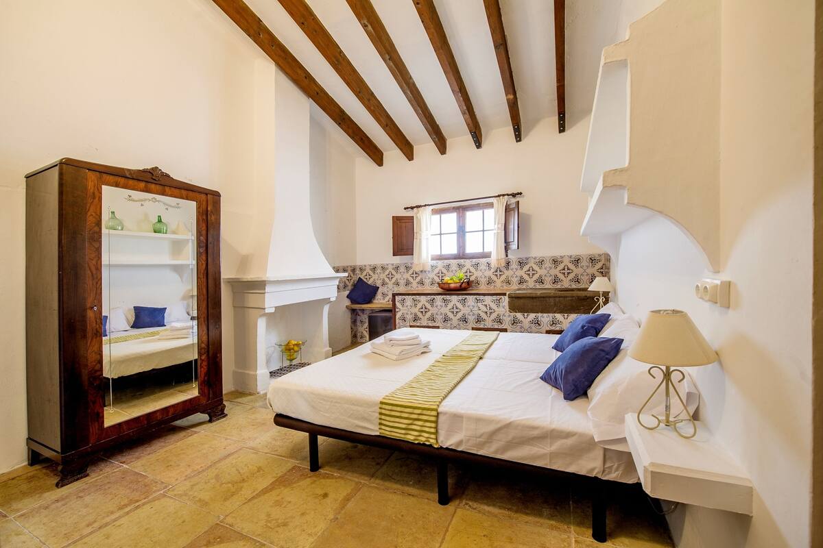 Une chambre à coucher avec un grand lit, une armoire en bois, une petite salle de bain et une fenêtre avec des rideaux.