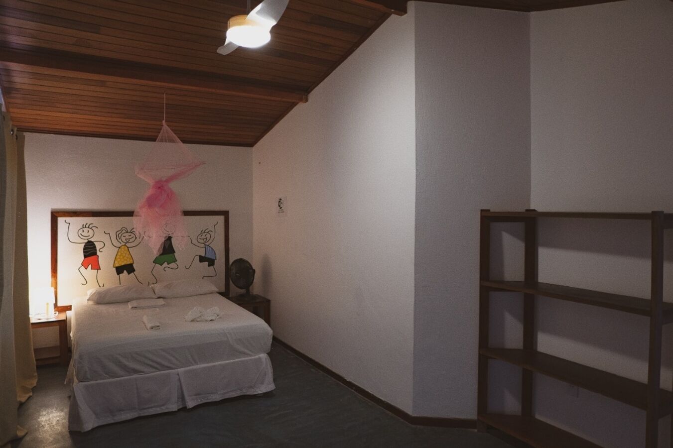 A bedroom with a bed, a wooden ceiling, a wall-mounted shelf, and a children's drawing on the wall.