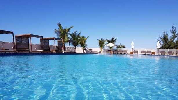 A clear blue pool with lounge chairs and palm trees. - Hotel Vila Jardim (Beberibe)