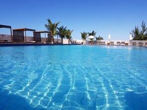 Ein klares, blaues Schwimmbecken mit Liegestühlen und Palmen.