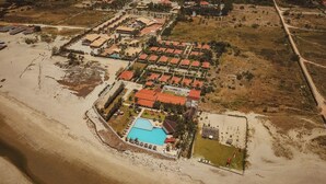 An aerial view of a resort with a central pool, multiple buildings with red roofs, and surrounding greenery. - Hotel Vila Jardim (Beberibe)