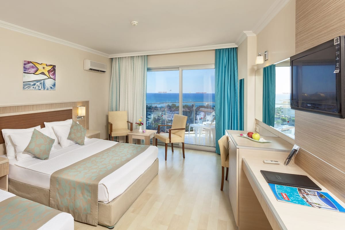 Habitación de hotel con dos camas, un escritorio, un televisor y un balcón con vistas al mar.
