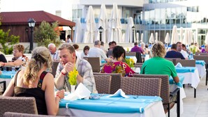 An outdoor dining area with wicker chairs and tables, a building with balconies in the background, and umbrellas. - Narcia Resort Side - All Inclusive (Manavgat)