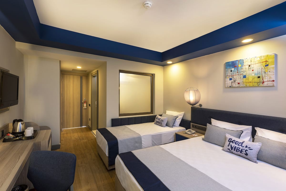 Habitación de hotel con dos camas, un escritorio con hervidor, una lámpara y un mapa en la pared.