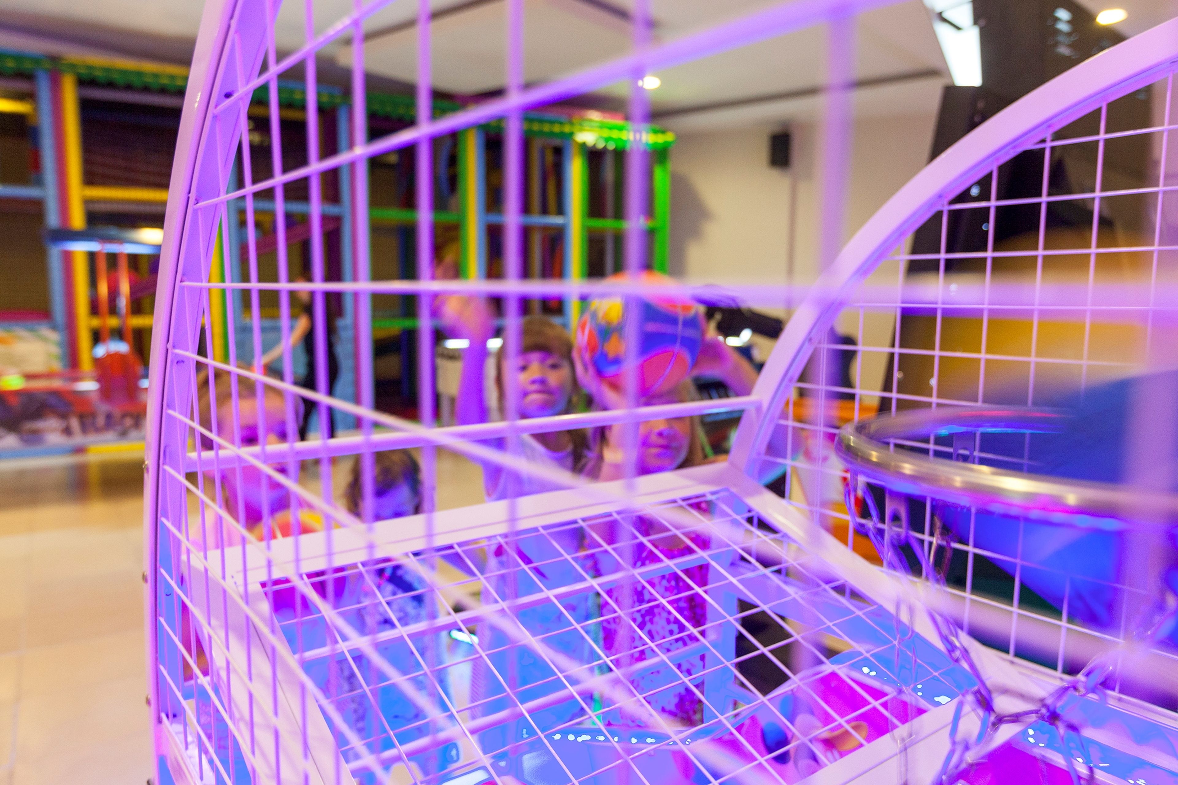 Un área de juegos interior, bien iluminada, con estructuras de juego coloridas y una barrera de seguridad púrpura.