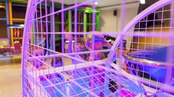 Un área de juegos interior, bien iluminada, con estructuras de juego coloridas y una barrera de seguridad púrpura.