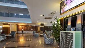 A modern hotel lobby with a reception desk, seating area, and a sign listing amenities like an indoor pool and fitness center. - Narcia Resort Side - All Inclusive (Manavgat)