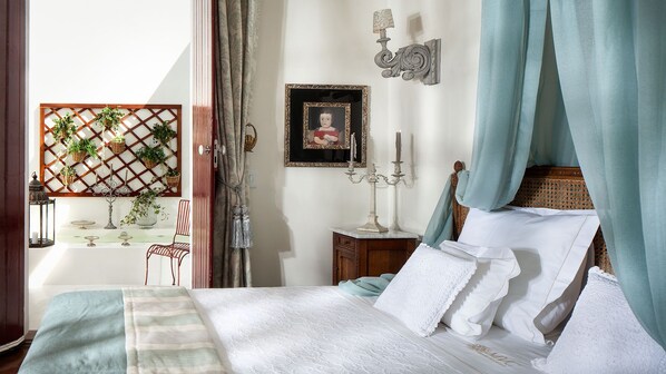 A bedroom with a bed, a nightstand, a wall-mounted lamp, a picture frame, and a window with curtains.